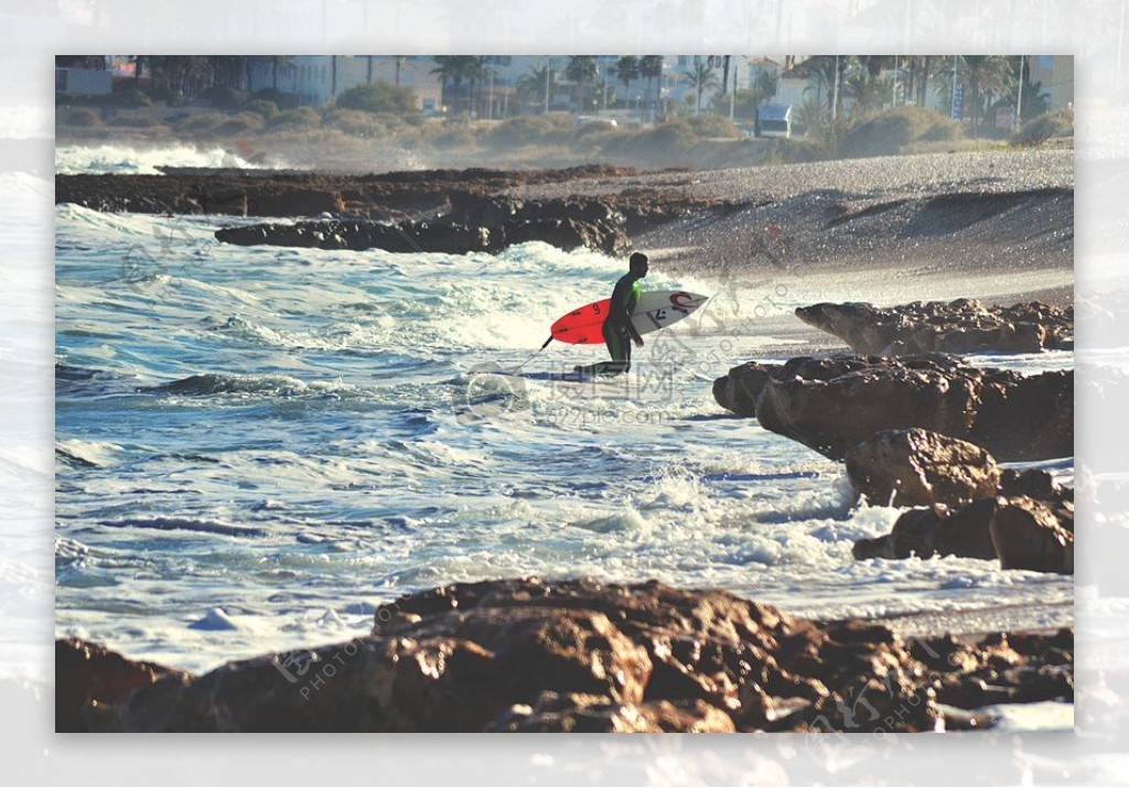 男子拿着红白冲浪板近海岸
