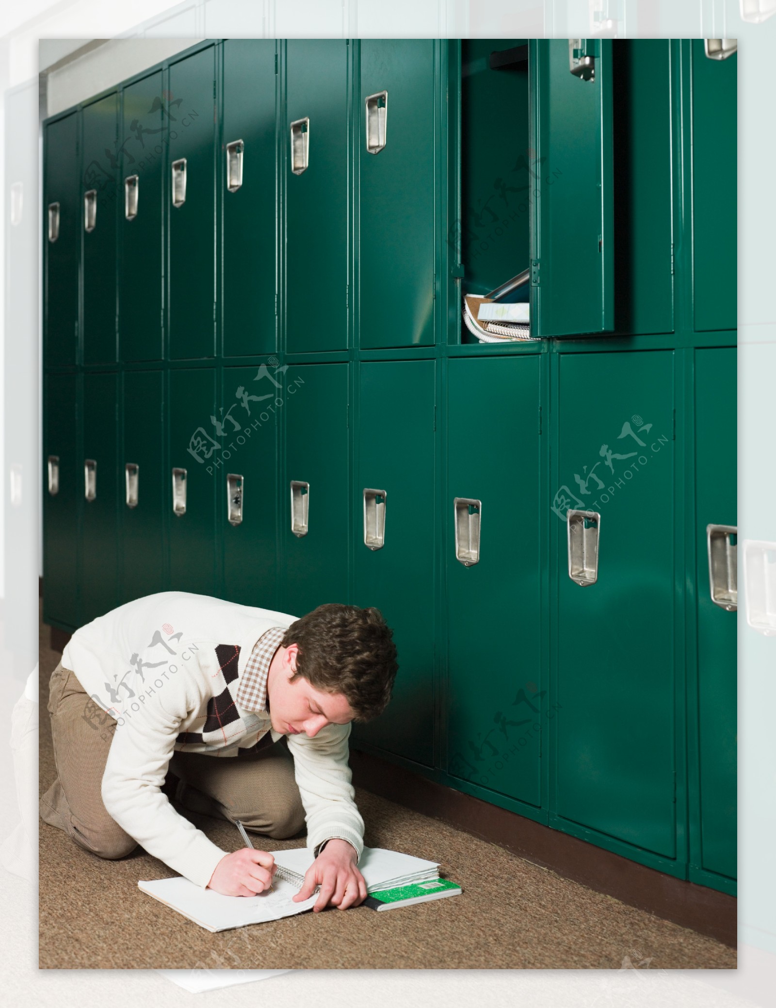 绿色储物柜旁跪在地上写字的男孩图片图片